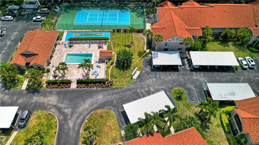 Aerial perspective showcasing community amenities including a tennis court, swimming pool, paved pool deck, and multiple covered parking structures