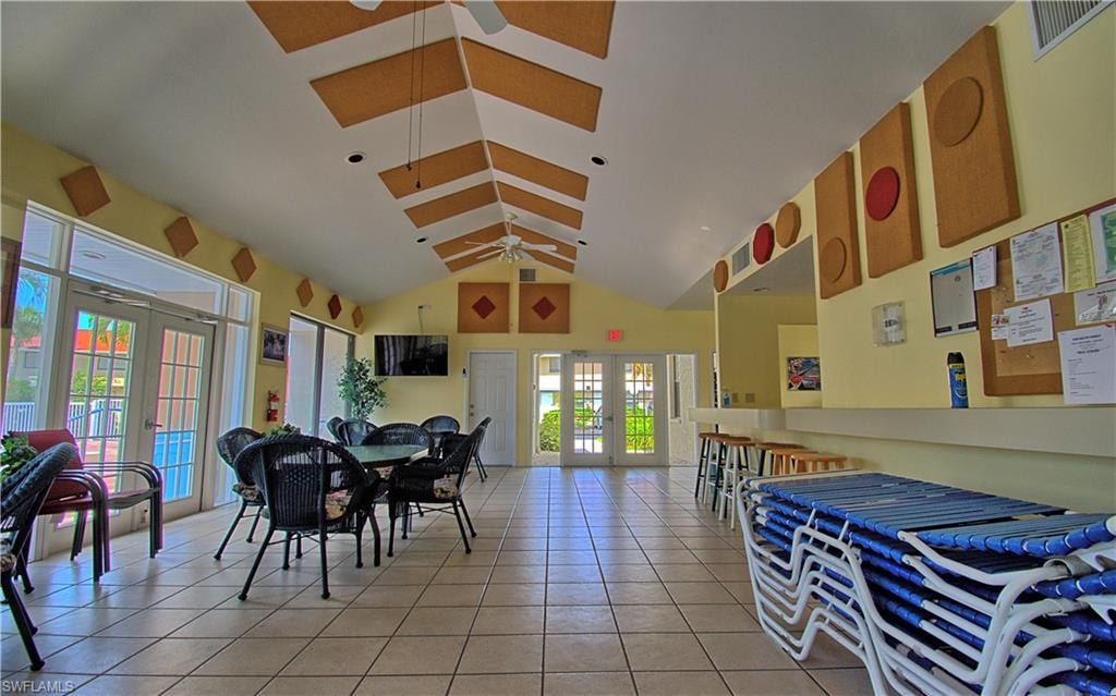 Spacious common area featuring vaulted ceilings with decorative panels, light tile flooring, multiple sets of French doors, and a built-in bar area with seating