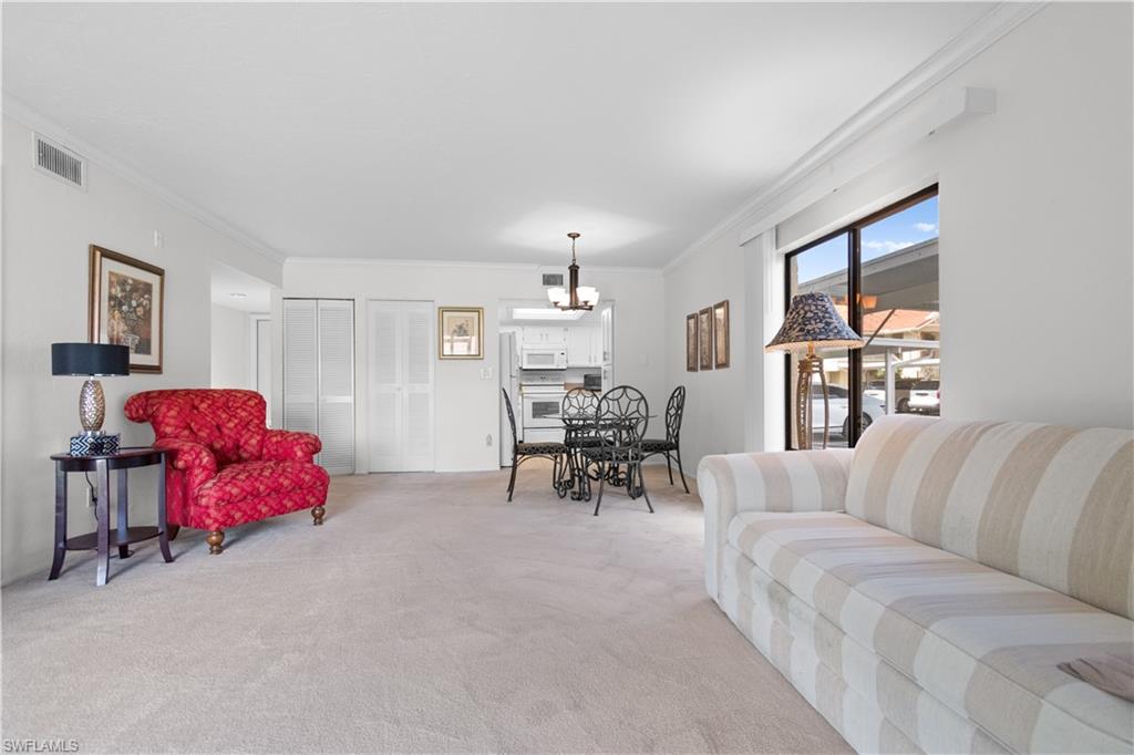 Spacious open-concept living area featuring light-colored carpeting, white walls, and crown molding