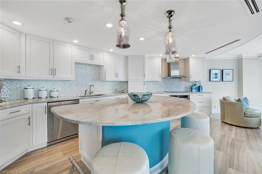Kitchen with wall chimney range hood, a breakfast bar area, stainless steel dishwasher, a sink, and white cabinets
