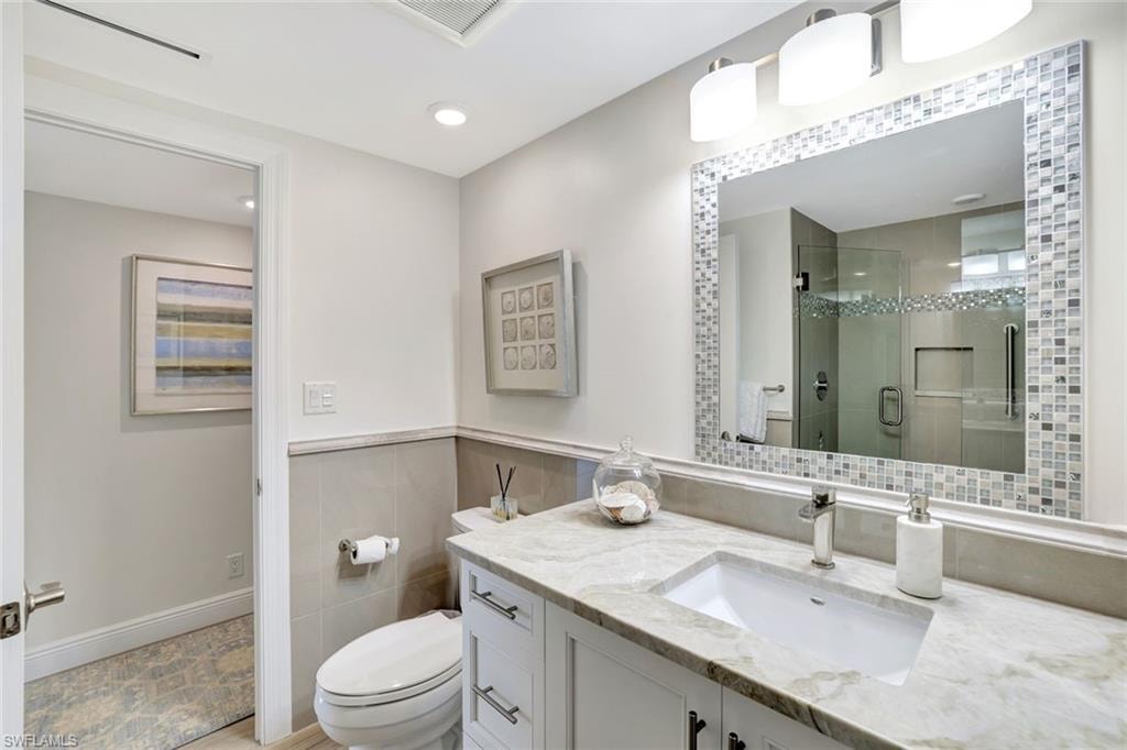 Full bath with vanity, toilet, tile walls, a shower stall, and visible vents