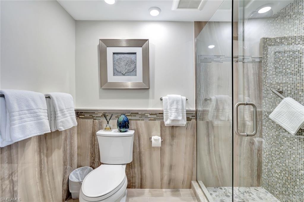 Full bath with tile walls, toilet, visible vents, and a stall shower