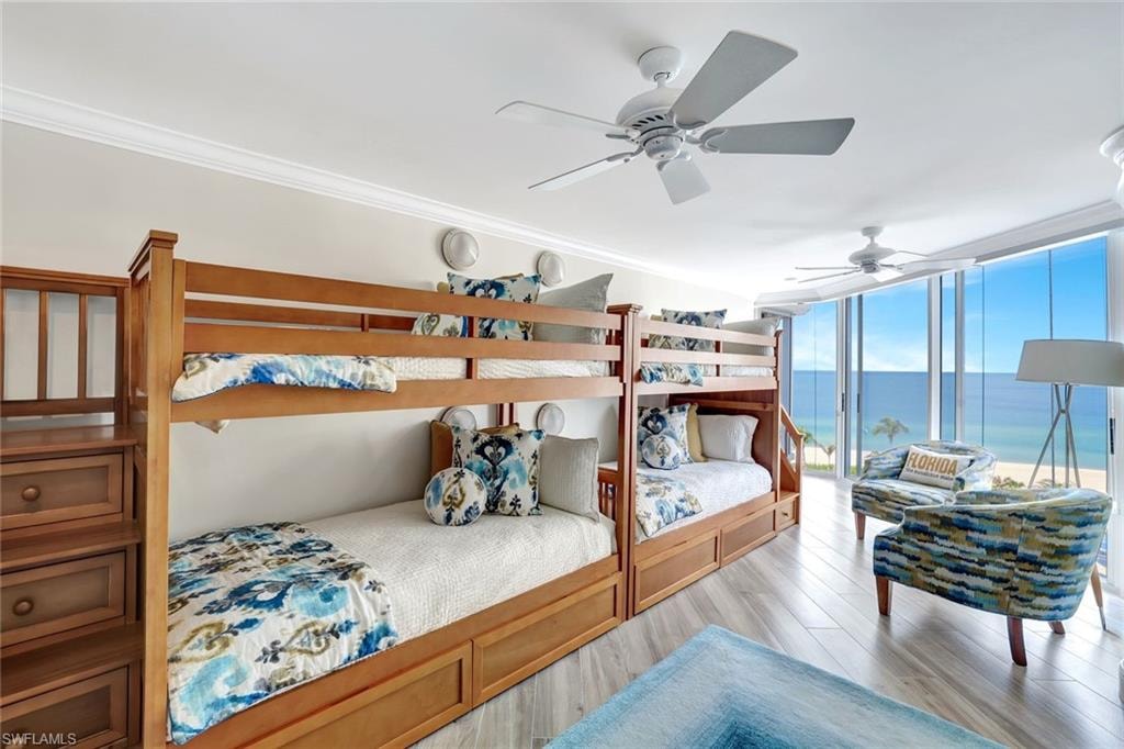 Bedroom featuring a wall of windows, a ceiling fan, crown molding, light wood-type flooring, and a water view