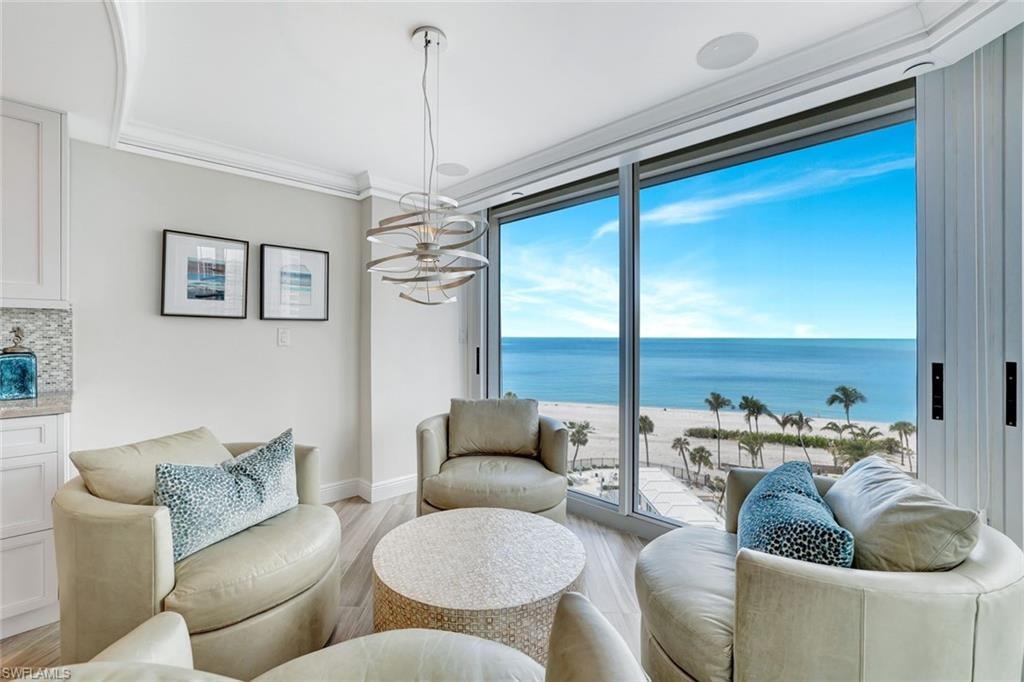 Living room featuring crown molding, an inviting chandelier, baseboards, light wood-type flooring, and a water view