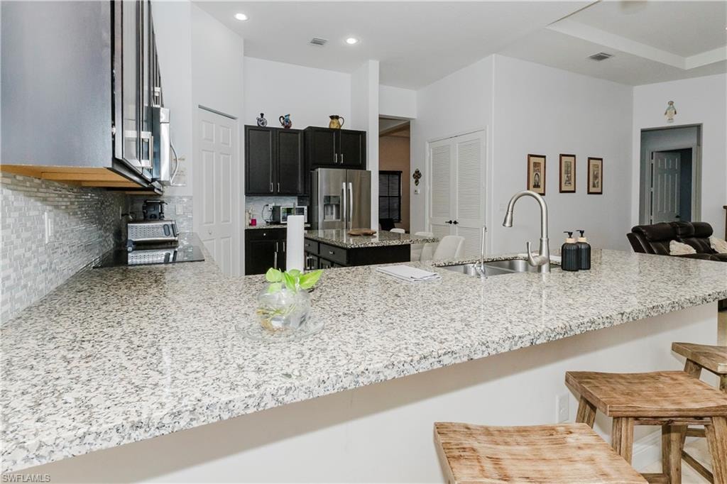 Kitchen with appliances with stainless steel finishes, backsplash, a center island, a breakfast bar, and a peninsula