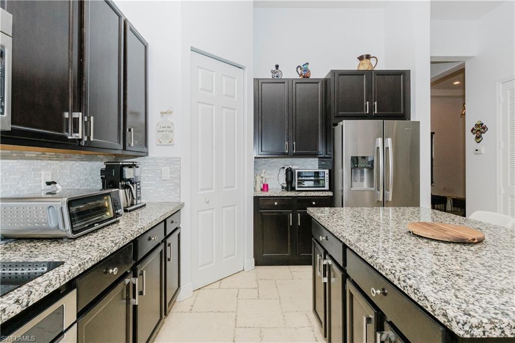 Kitchen featuring stainless steel fridge with ice dispenser, stone tile flooring, decorative backsplash, light stone countertops, and a kitchen island