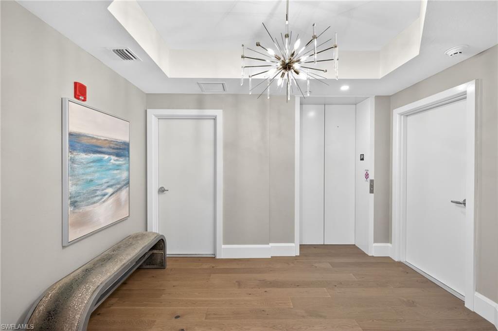 Large foyer entrance off elevator is welcoming with light wood floors and stylish chandelier
