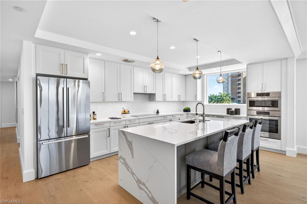 Stunning kitchen with stainless steel appliances, hanging light fixtures, a large kitchen island with sink, and recessed lighting