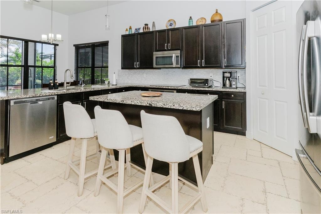 Kitchen with appliances with stainless steel finishes, a chandelier, a breakfast bar, a kitchen island, and hanging light fixtures