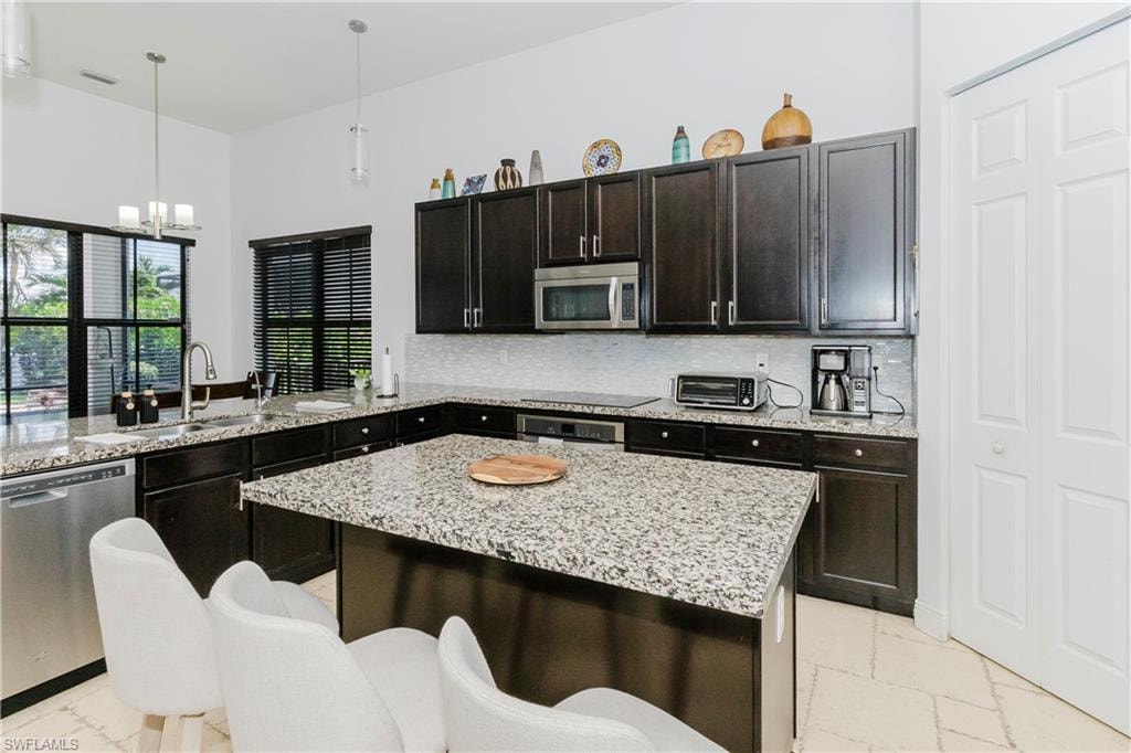 Kitchen with stainless steel appliances, a chandelier, pendant lighting, and light stone counters