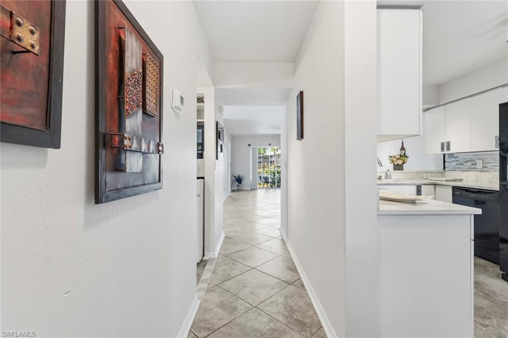Hallway featuring diagonal tile flooring, white walls, and a partial view of a kitchen with white cabinetry and a light-colored countertop