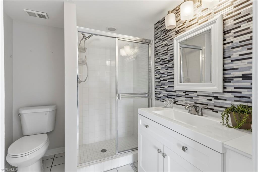 Bathroom featuring a NEW toilet, glass-enclosed shower, white vanity with integrated sink, contemporary mosaic tile accent wall, framed mirror, and chrome fixtures