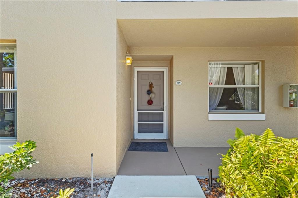 Warm beige stucco exterior with a covered entry, screened storm door, and decorative outdoor lighting fixture