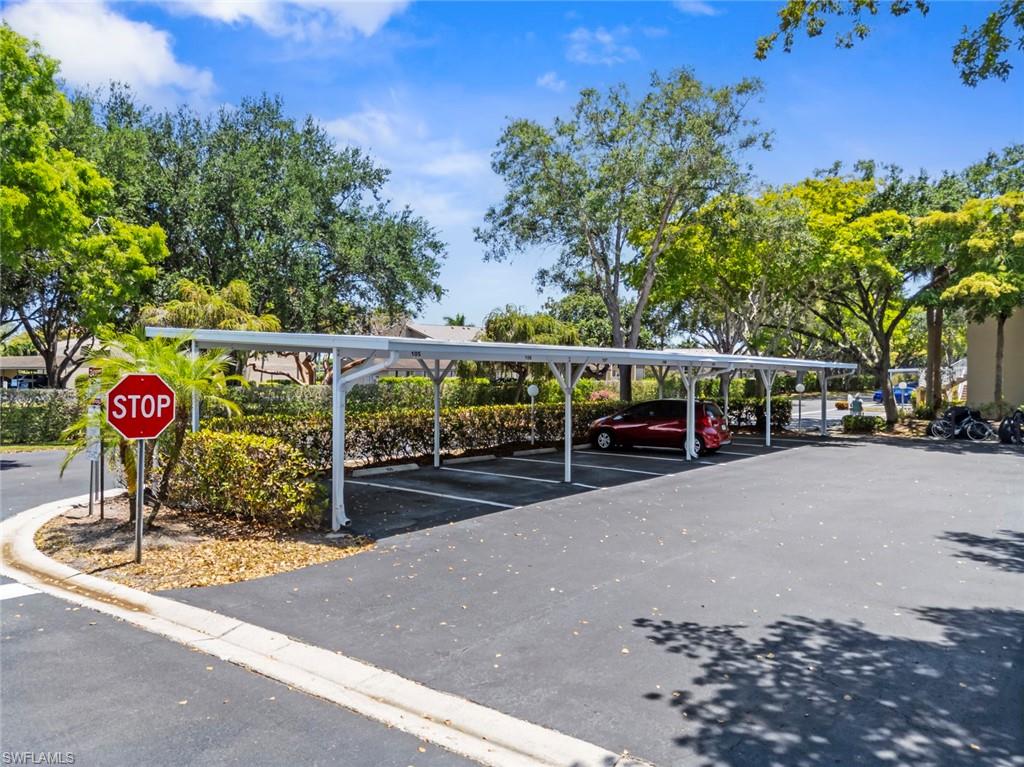 Covered parking structure with multiple spaces, featuring a white metal frame and asphalt pavement