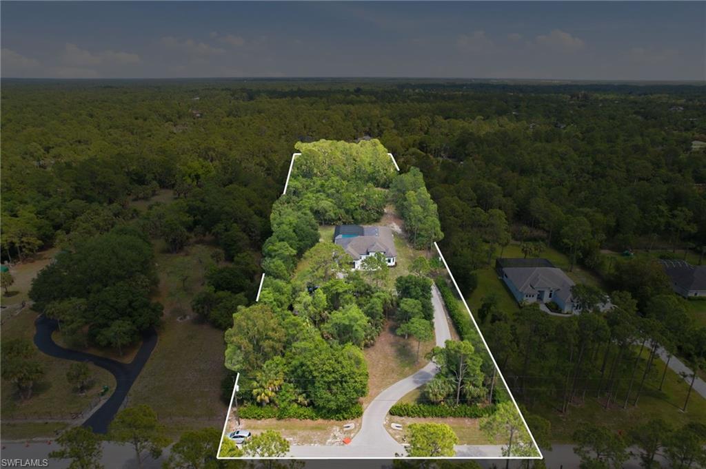 Aerial view showcasing a substantial parcel of land, featuring mature trees and a main residence with a light-colored roof