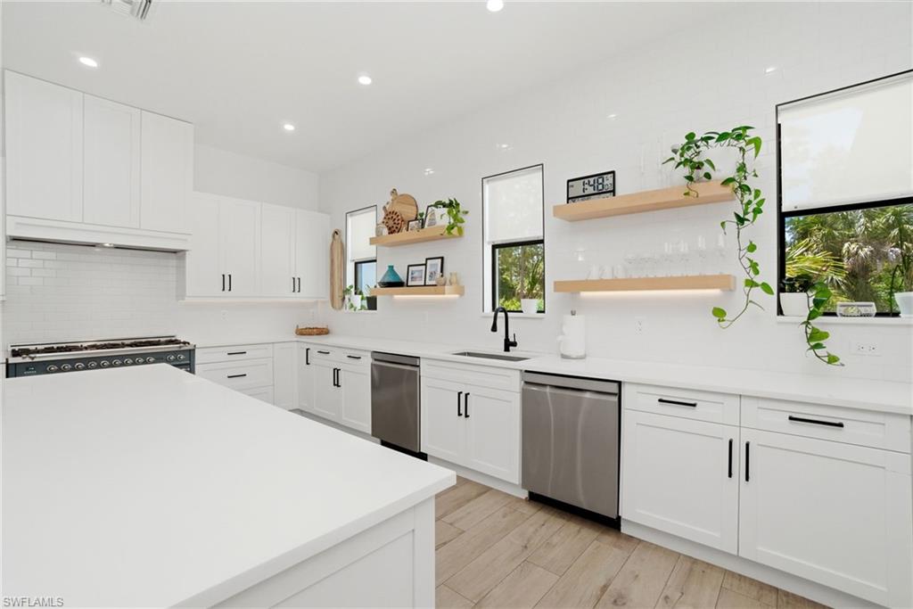 Spacious kitchen featuring white cabinetry, light countertops, subway tile backsplash, stainless steel appliances, and wood-finish flooring