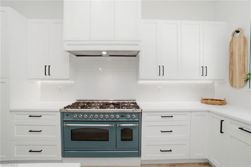 Gourmet kitchen featuring a striking teal range, white shaker-style cabinetry, white countertops, a white subway tile backsplash, and dark hardware