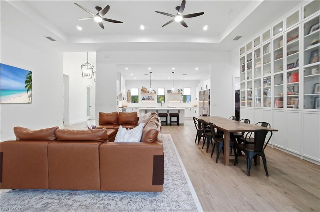 Open-concept living space featuring wood-finish flooring, recessed lighting, ceiling fans, and a full wall of built-in cabinetry with glass-front uppers
