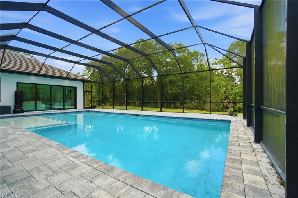 Screened pool enclosure featuring a rectangular pool, integrated spa, and paver decking