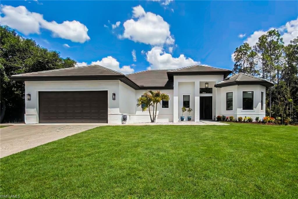 Contemporary stucco exterior with a dark tile roof, an integrated two-car garage, manicured front lawn, and surrounding natural landscaping