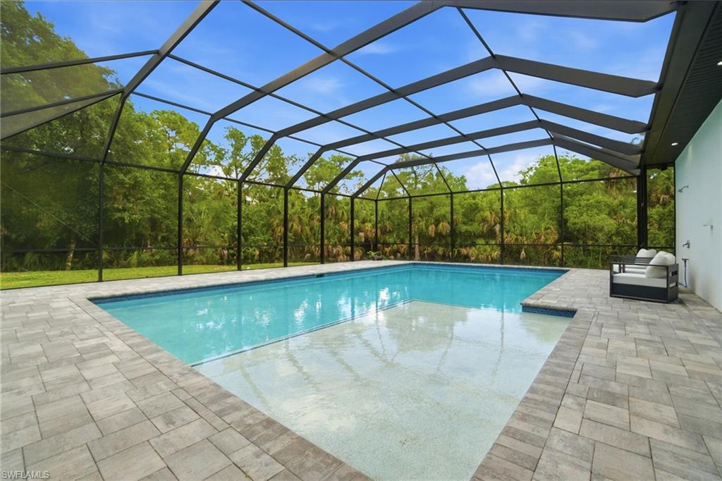 Screened-in swimming pool featuring a paver patio surround, integrated sun shelf, and a perimeter of mature trees beyond the enclosure