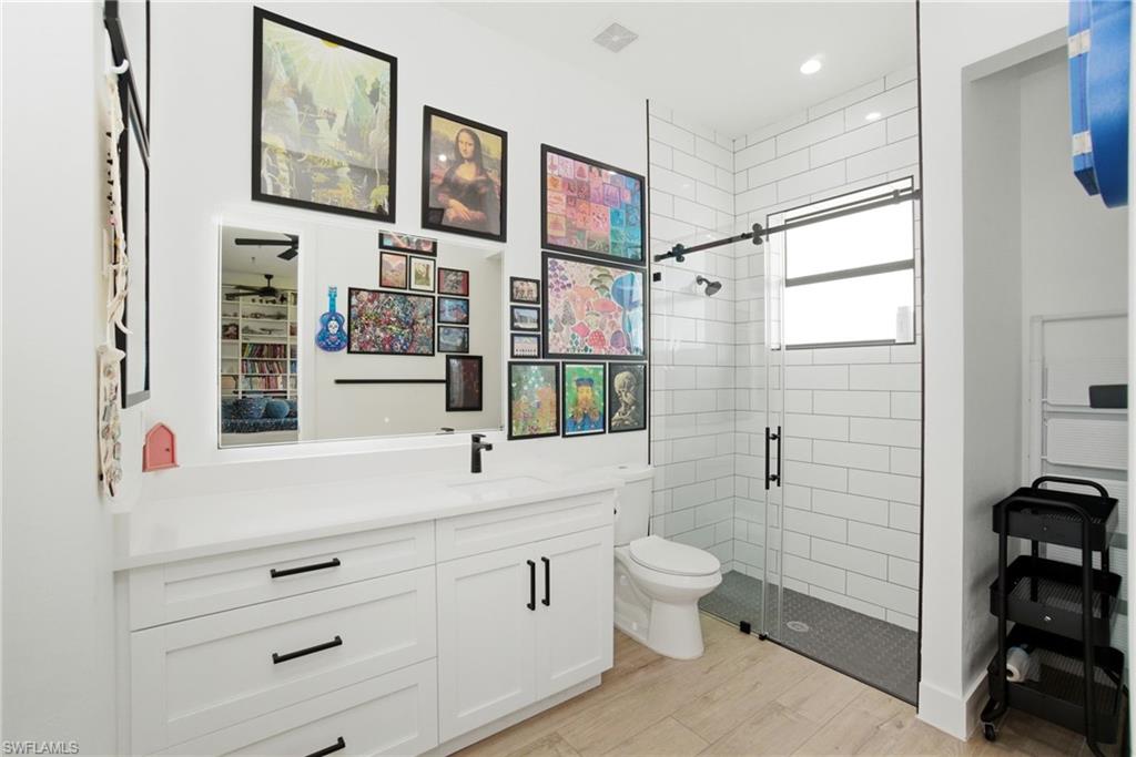 Modern bathroom featuring a white vanity with integrated sink, sleek black fixtures, a spacious glass-enclosed shower with subway tile surround, a privacy window, and wood-finish flooring