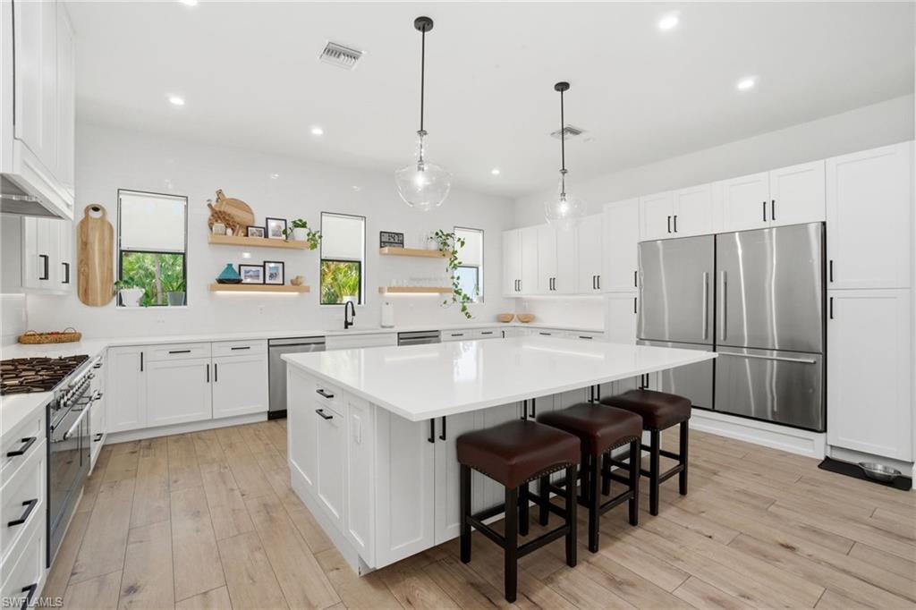 Spacious kitchen featuring an expansive central island with seating, white shaker cabinetry, stainless steel appliances, and light wood-finish flooring