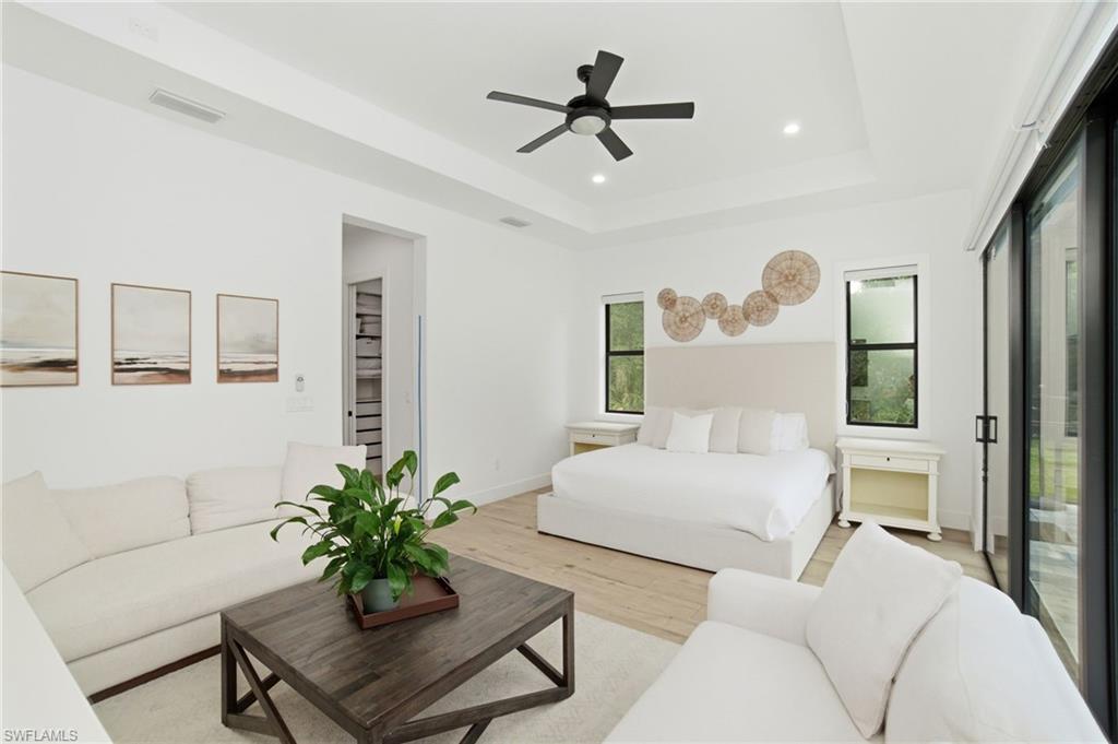 Spacious bedroom featuring wood-finish flooring, a tray ceiling with a ceiling fan, recessed lighting, and large sliding glass doors