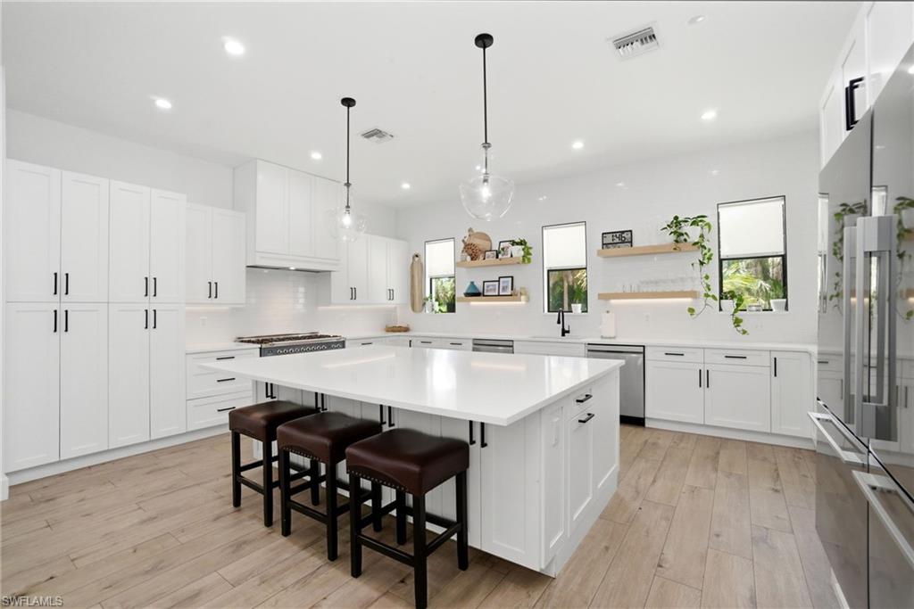 Spacious kitchen featuring an expansive central island with seating, extensive white cabinetry, light wood-finish flooring, recessed lighting, and stainless steel appliances