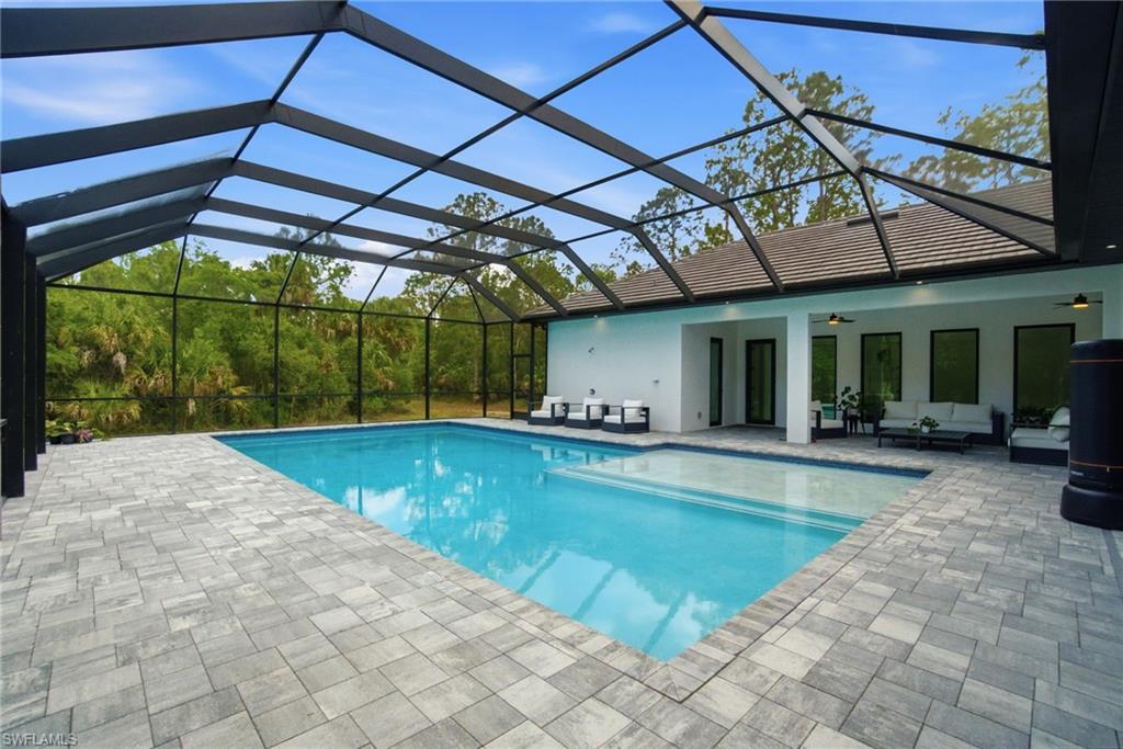 Screened enclosure featuring a rectangular swimming pool with integrated steps, surrounded by gray paver decking