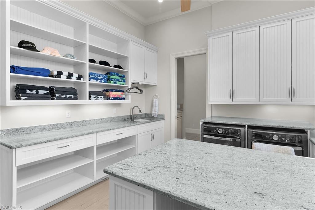 Spacious laundry area featuring extensive white cabinetry, granite countertops, an undermount sink, and a large central island