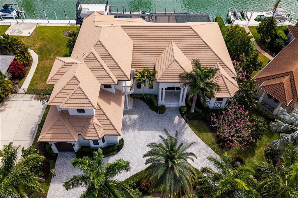 Waterfront residence featuring a terracotta-tiled roof, mature palm trees, a circular driveway, and a private dock