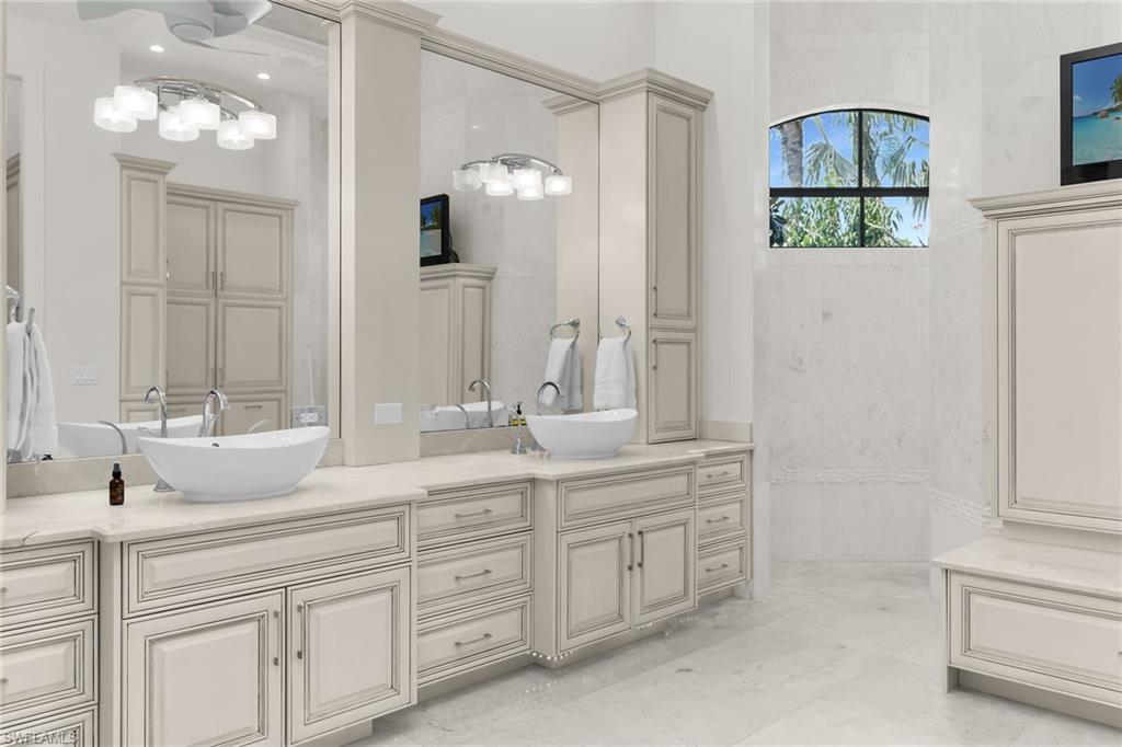 Dual vanity featuring vessel sinks, light-toned cabinetry, light-colored countertops, large mirrors, and a decorative arched window