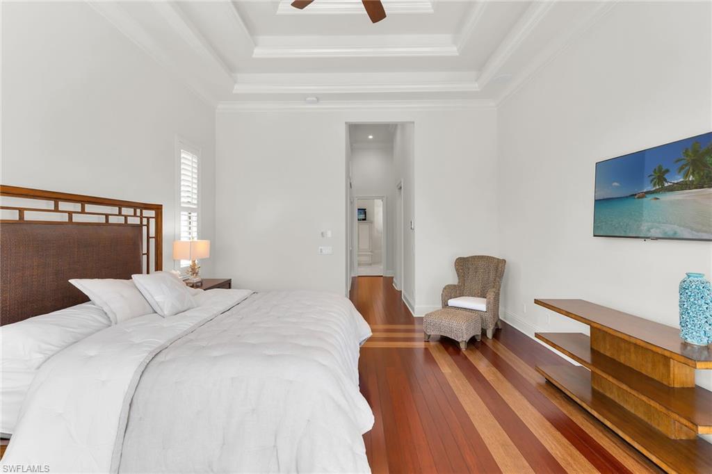 Spacious room featuring rich wood-finish flooring with contrasting tones, a multi-tiered tray ceiling, and crisp white walls