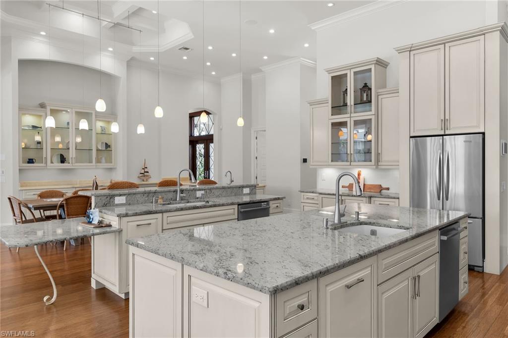 Gourmet kitchen featuring multiple granite-top islands, stainless steel appliances, extensive cabinetry with glass display fronts, recessed lighting, and hardwood flooring