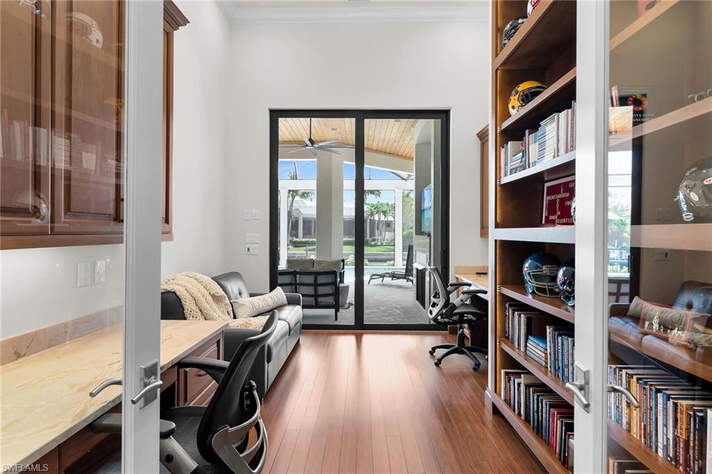 Private office space featuring wood-finish flooring, tall ceilings, built-in shelving, and a large sliding glass door opening to an outdoor living area
