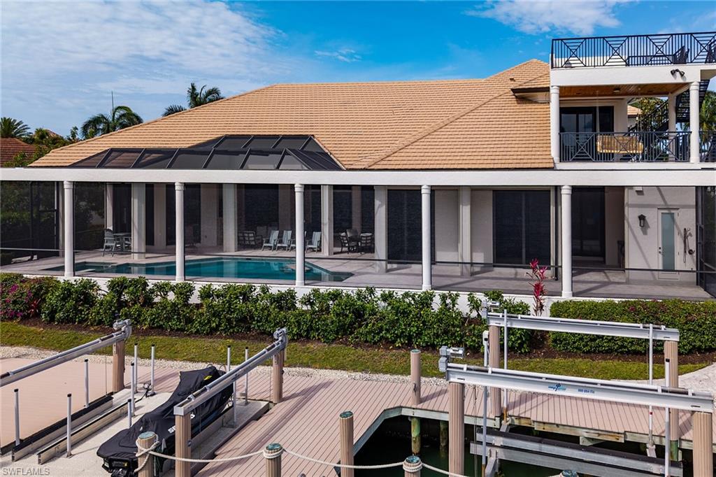 Waterfront residence featuring a screened-in pool and spa, multiple boat lifts, an upper-level balcony, and a rooftop deck