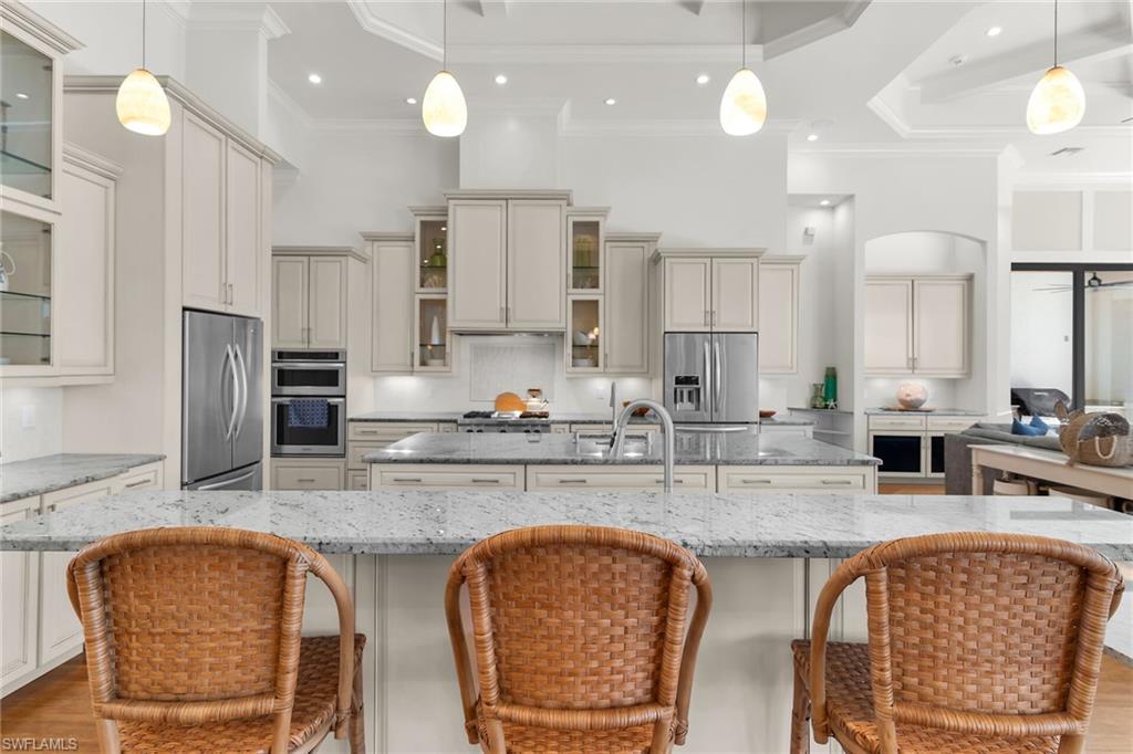 Spacious kitchen featuring a large island with a stainless steel sink, light-toned cabinetry, stainless steel appliances, recessed lighting, and a tray ceiling with pendant lighting