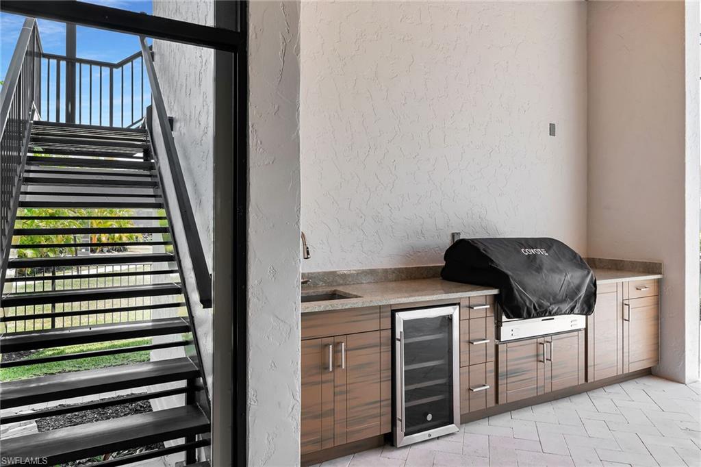 Outdoor kitchen featuring wood-finish cabinetry, stone countertop, built-in grill, and beverage refrigerator