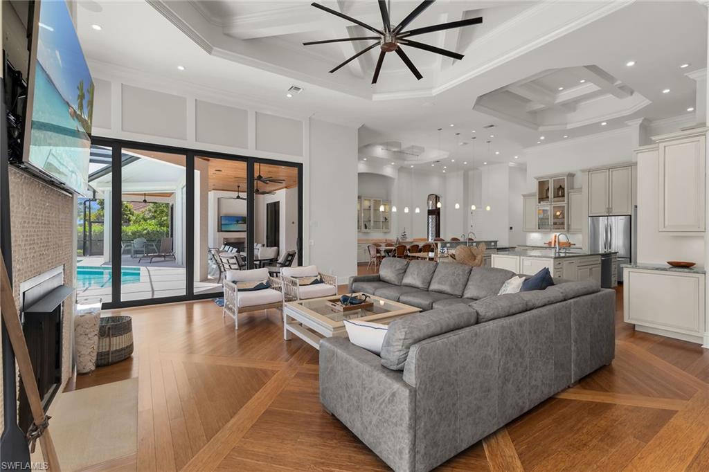 Spacious living area featuring coffered ceilings, wood-finish flooring with a distinctive pattern, and expansive sliding glass doors