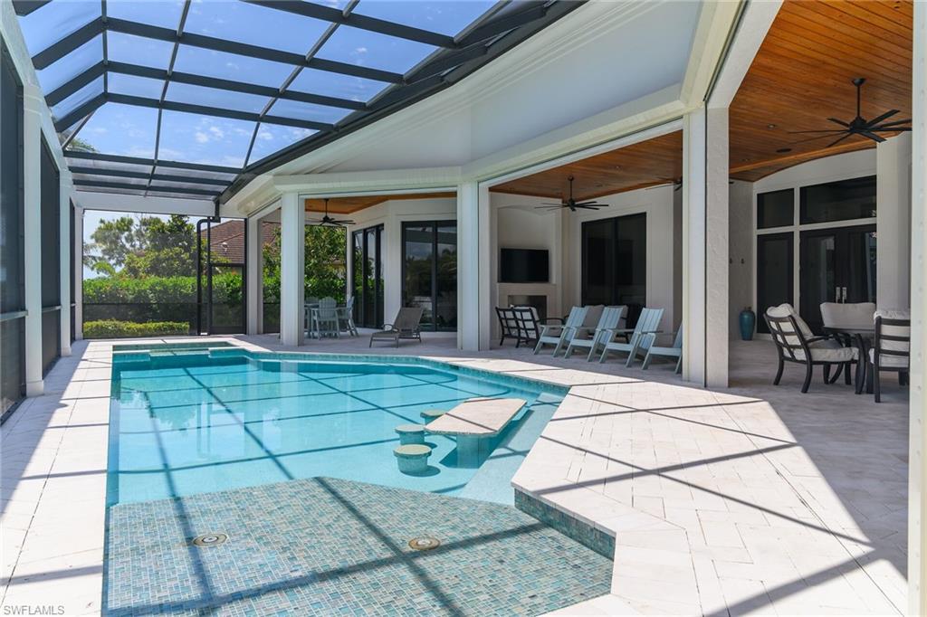 Screened outdoor living area featuring a rectangular pool with an in-pool seating area, a mosaic-tiled spa, and a light-toned paver deck