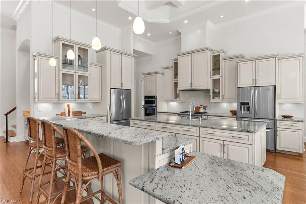 Expansive kitchen featuring a large central island, light-toned cabinetry, stainless steel appliances, pendant lighting, and wood-finish flooring