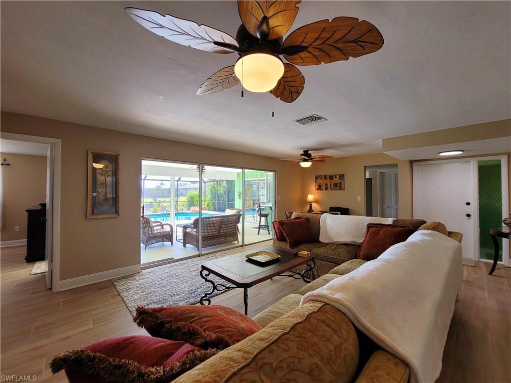 Open concept living area featuring wood-finish flooring, a tropical-style ceiling fan, and sliding glass doors leading to an outdoor screened patio with a pool