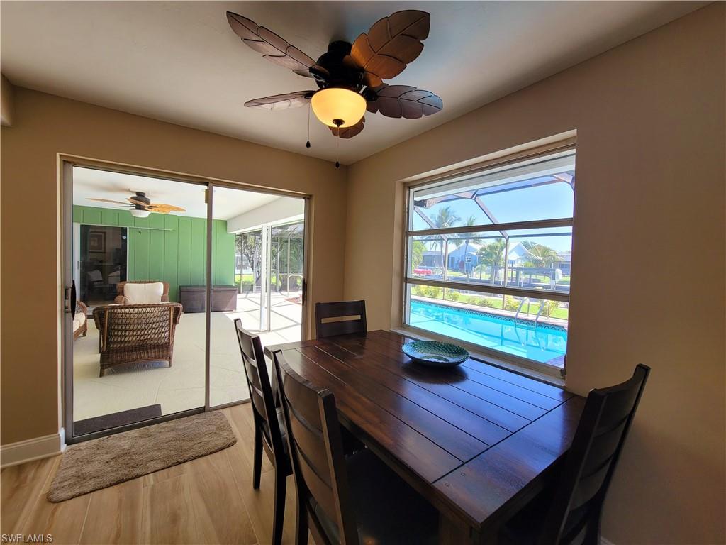 Dining area featuring wood-finish flooring, a decorative ceiling fan with integrated lighting, and a window overlooking a swimming pool