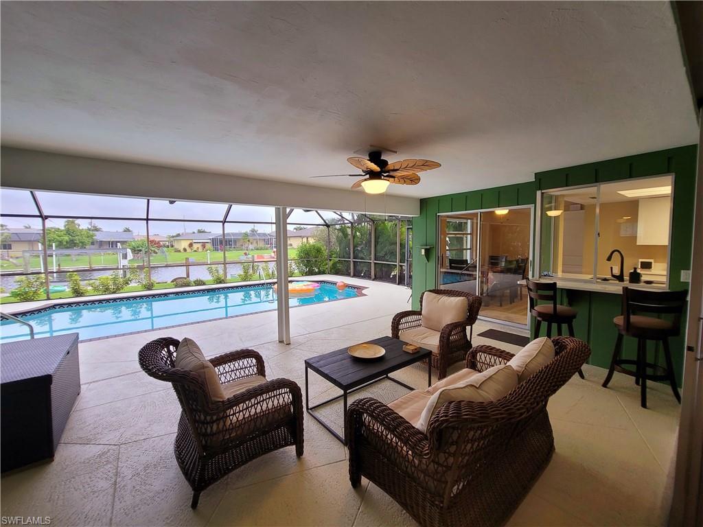 Screened-in lanai featuring a swimming pool, textured concrete patio, ceiling fan, and a pass-through bar