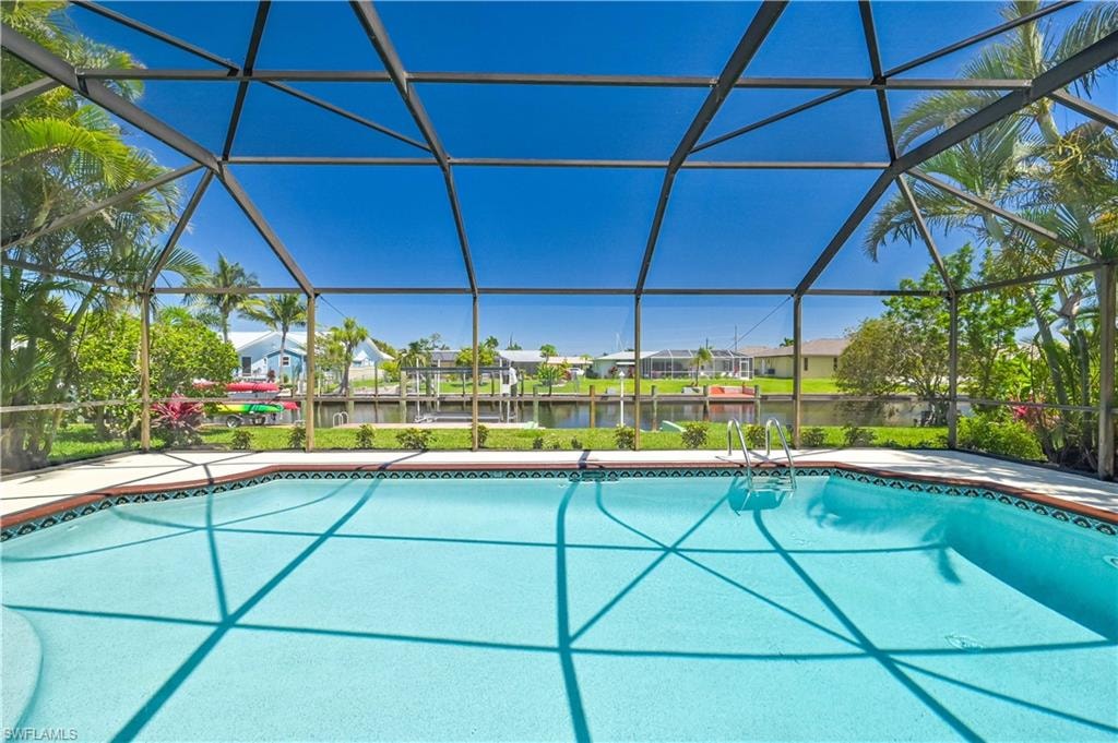 Screened swimming pool with a tile border and steps, surrounded by mature landscaping and a canal beyond