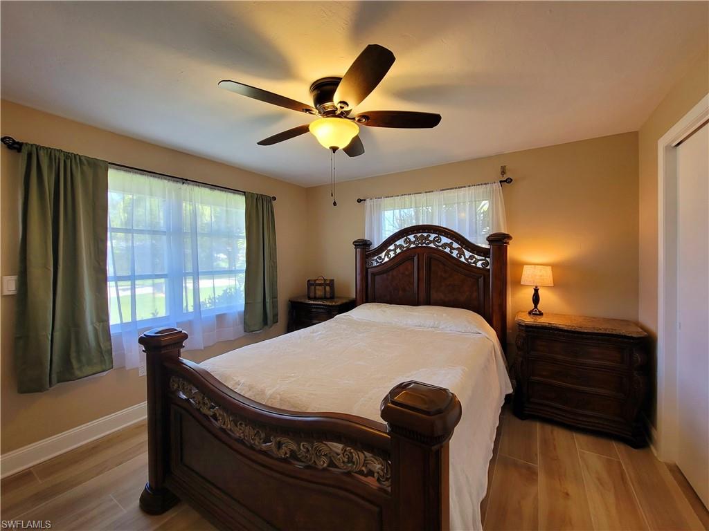 Interior room featuring wood-finish flooring, a ceiling fan with integrated lighting, and a window with white window treatments and green drapes