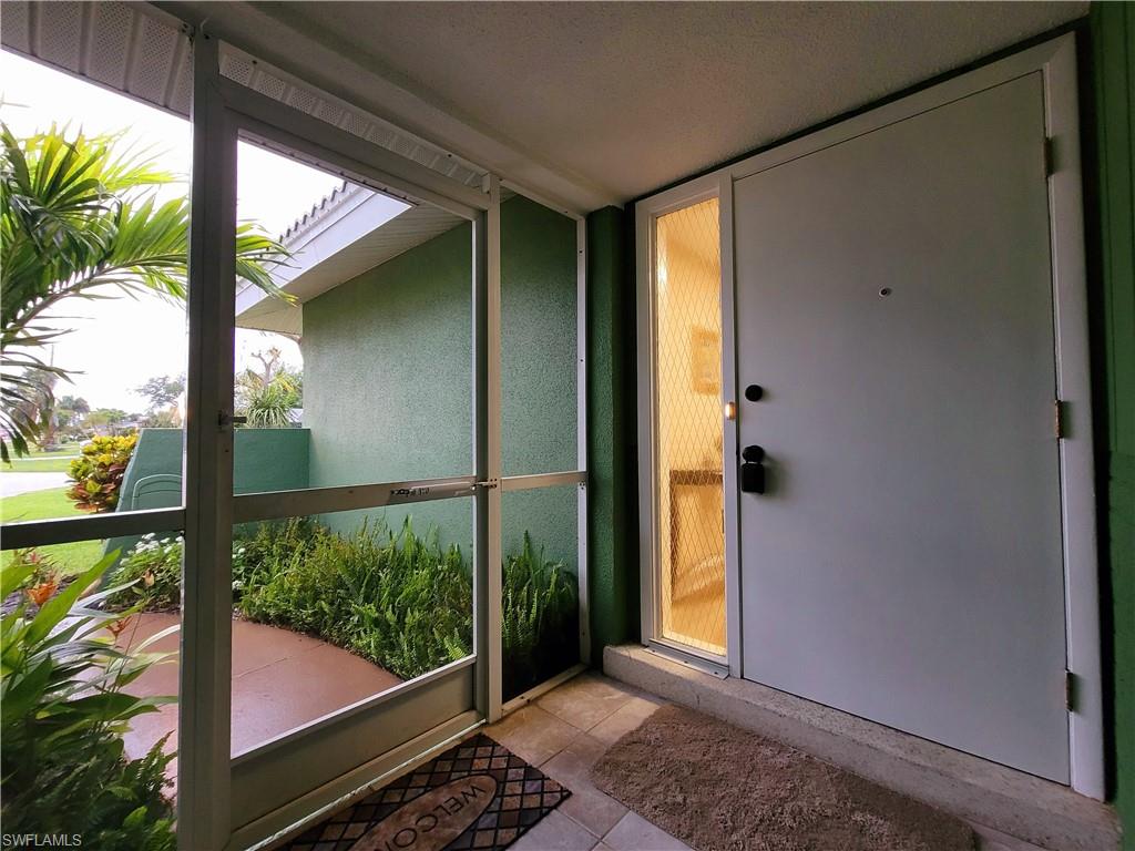 Entryway featuring a white door with a glass sidelight, screened porch enclosure, exterior wall with stucco finish, and tile flooring