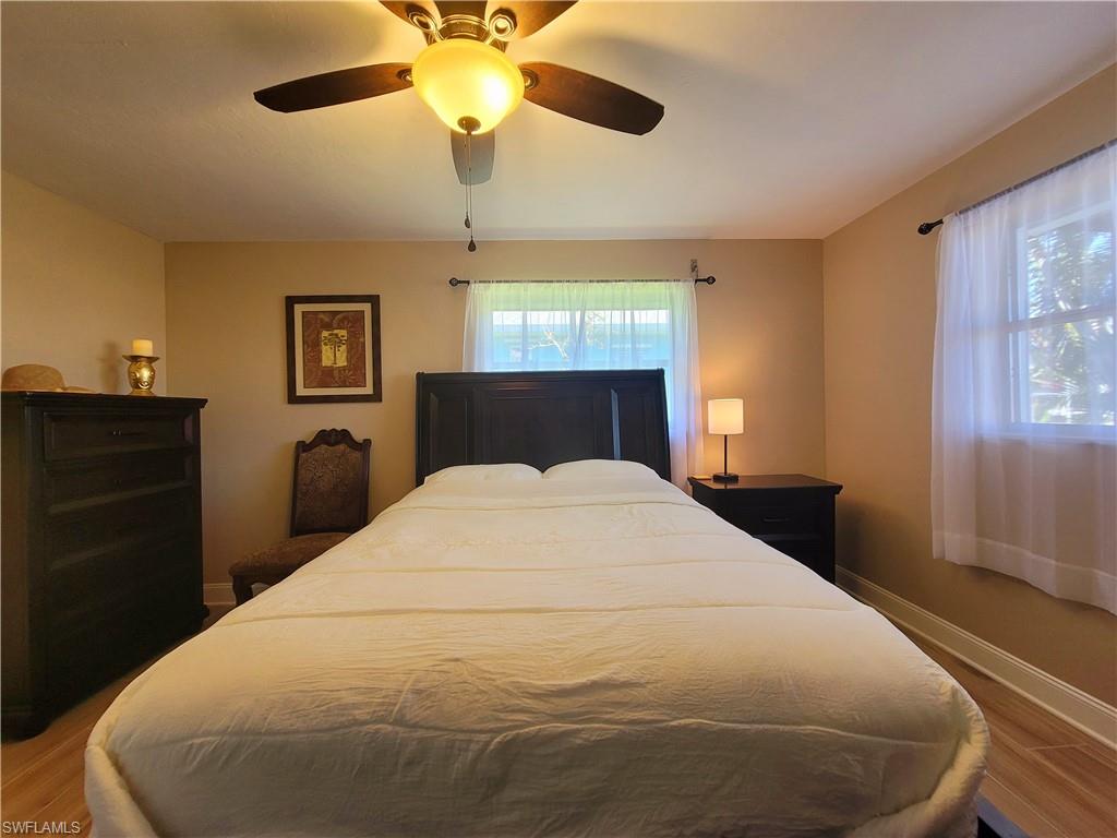 Bedroom featuring a ceiling fan, two windows with sheer curtains, neutral wall paint, and wood-finish flooring