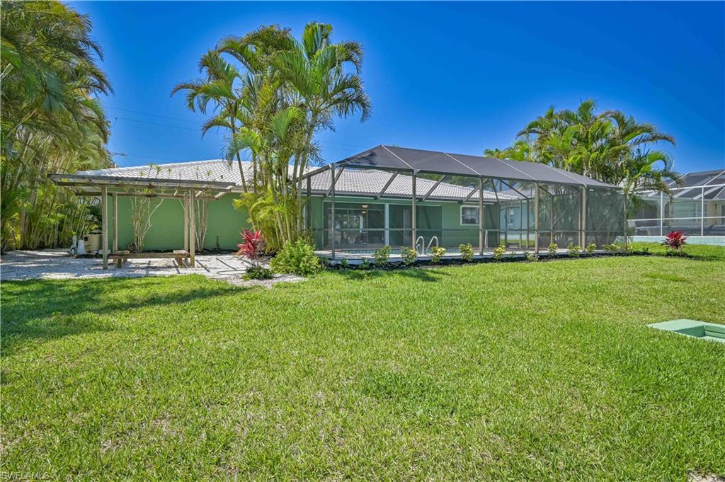Expansive green lawn featuring a screened pool enclosure, a wooden pergola, and established palm trees